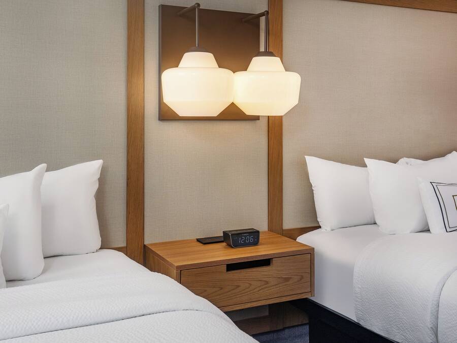 Une chambre d’hôtel avec deux lits, une table de chevet avec une horloge et un luminaire fixé au mur.