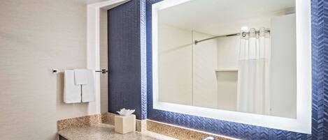 A bathroom with a large mirror, a granite countertop, a sink, and a towel rack.
