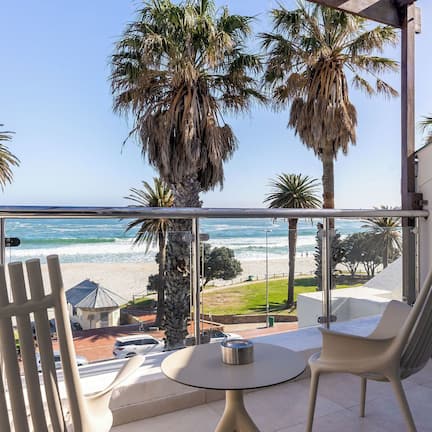 A balcony with a view of the beach and ocean, featuring two chairs and a small table.