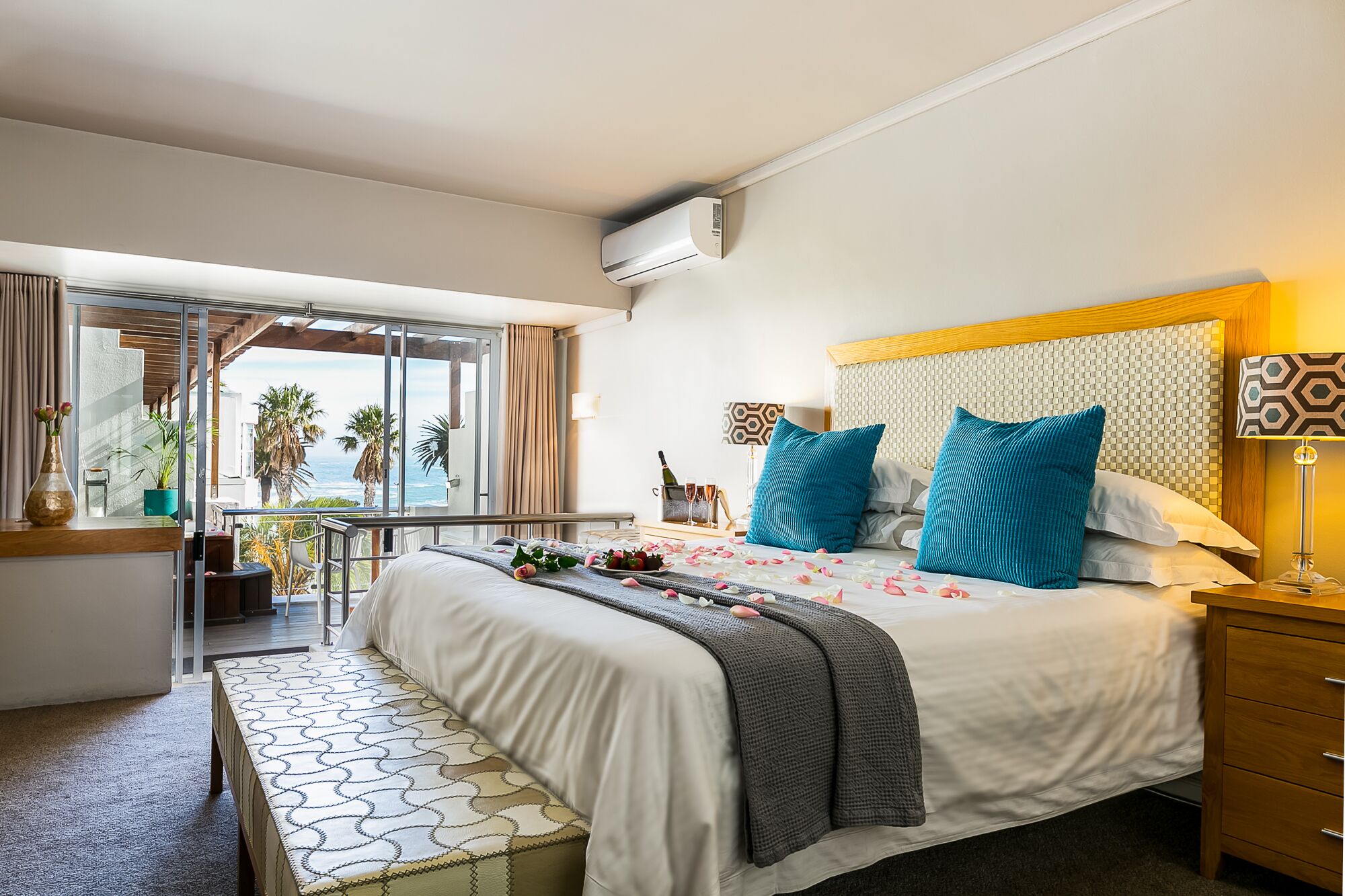 Habitación de hotel con cama, mesita de noche, lámpara y vista al océano.