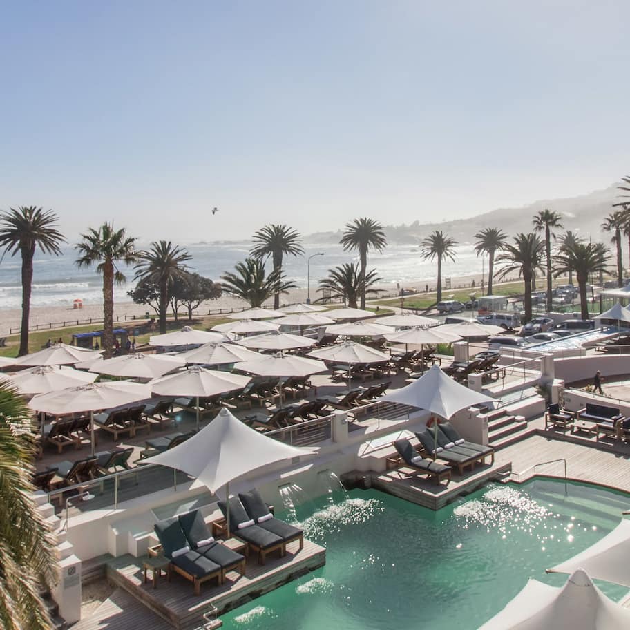 A resort with a pool area, lounge chairs, umbrellas, and a view of the beach and ocean.