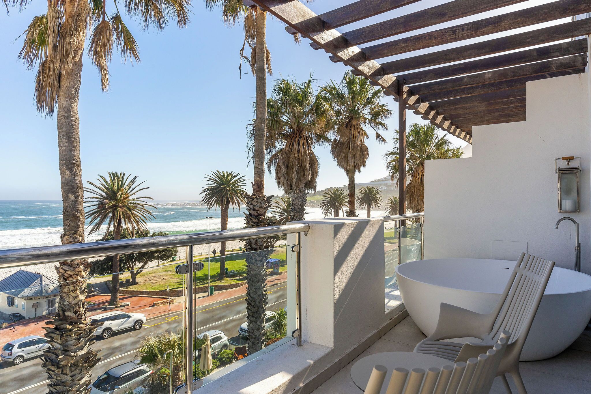 A balcony with a view of the ocean, a large bathtub, and a modern chair.