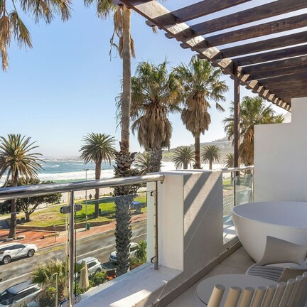 A balcony with a view of the ocean, a large bathtub, and a modern chair.