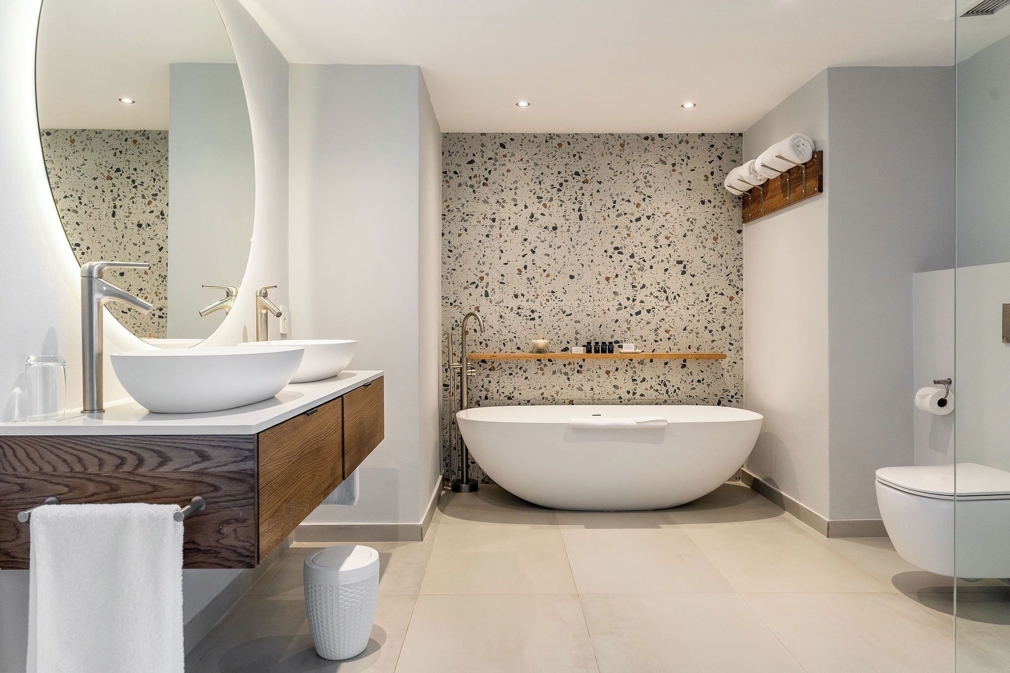 Un baño moderno con una bañera independiente, un espejo grande y un mueble de tocador de madera.