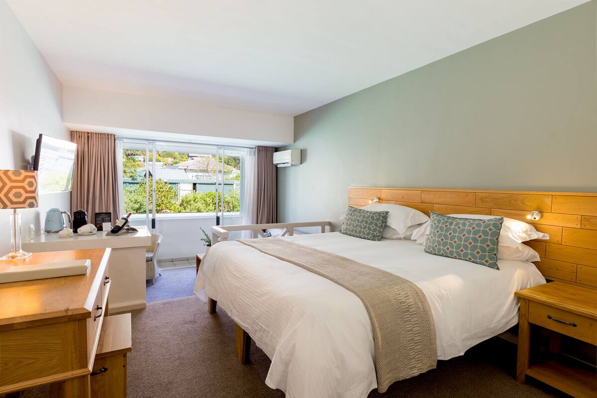 Ein Hotelzimmer mit einem großen Bett, einem Schreibtisch, einem Sessel, einem Nachttisch und einem Fenster mit Vorhängen.
