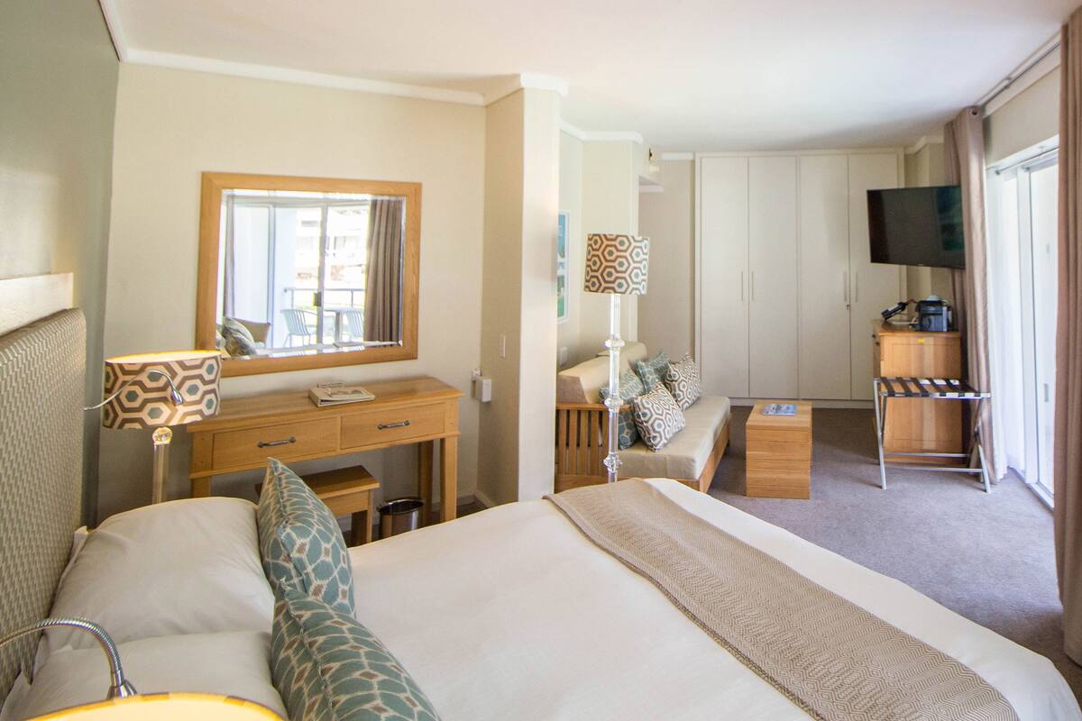 Ein Hotelzimmer mit einem großen Bett, einem Schreibtisch mit Lampe, einem Fernseher und einem Kleiderschrank.
