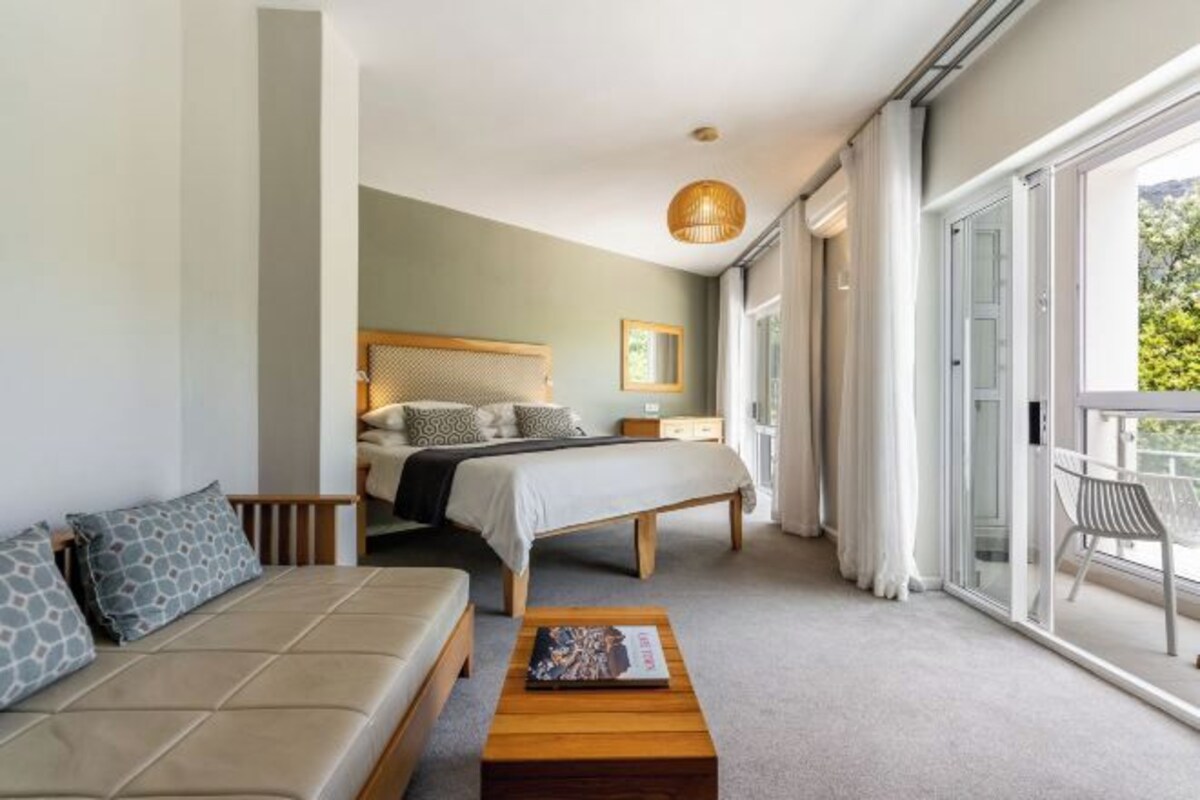 A modern hotel room with a bed, a sofa, a coffee table, and a balcony with a view.