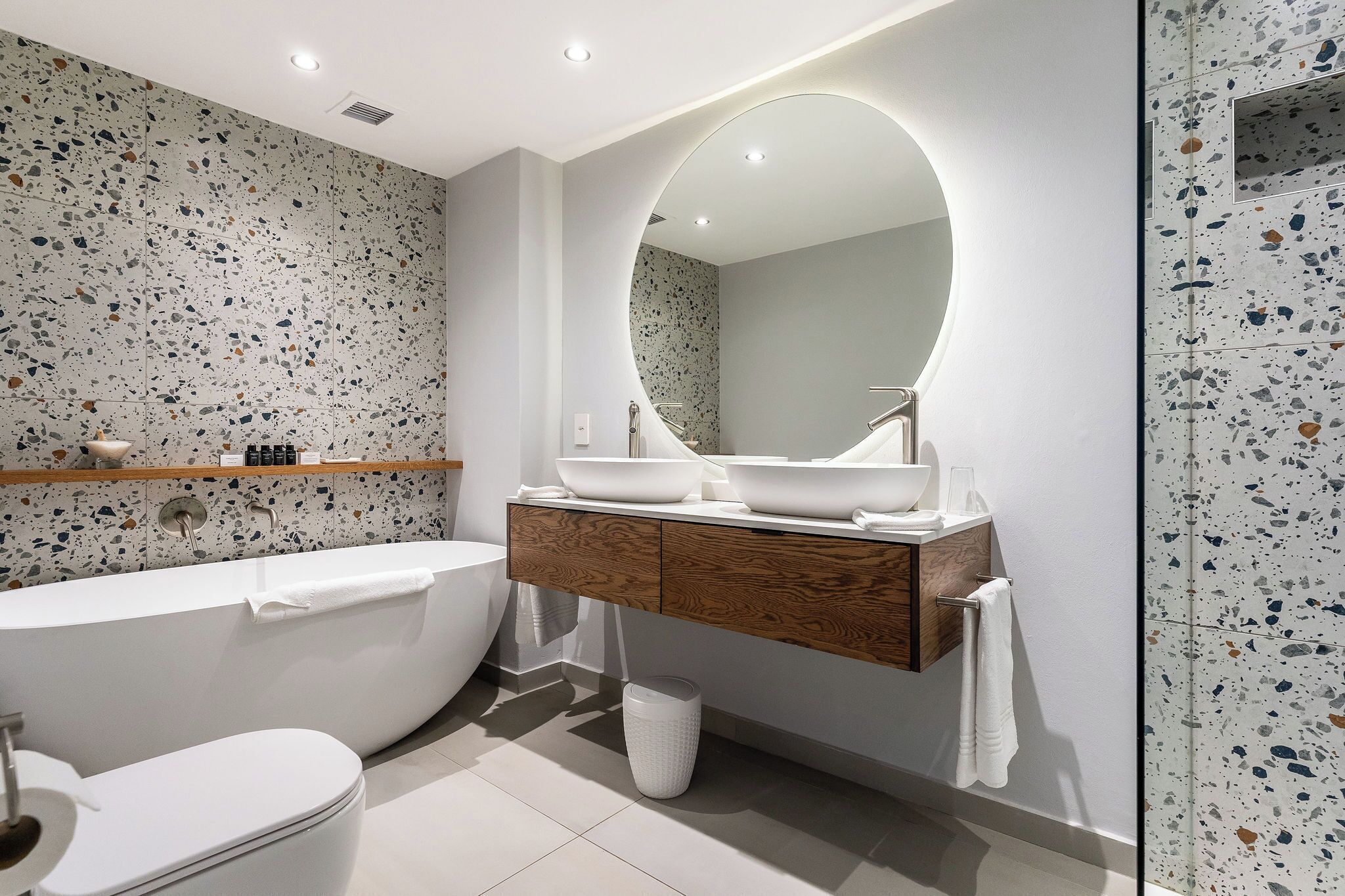 A modern bathroom with a freestanding bathtub, a wooden vanity with a large mirror, and a tiled backsplash.