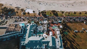 An aerial view of a coastal hotel with a beach, parking area, and pool. - The Bay Hotel (Cape Town)