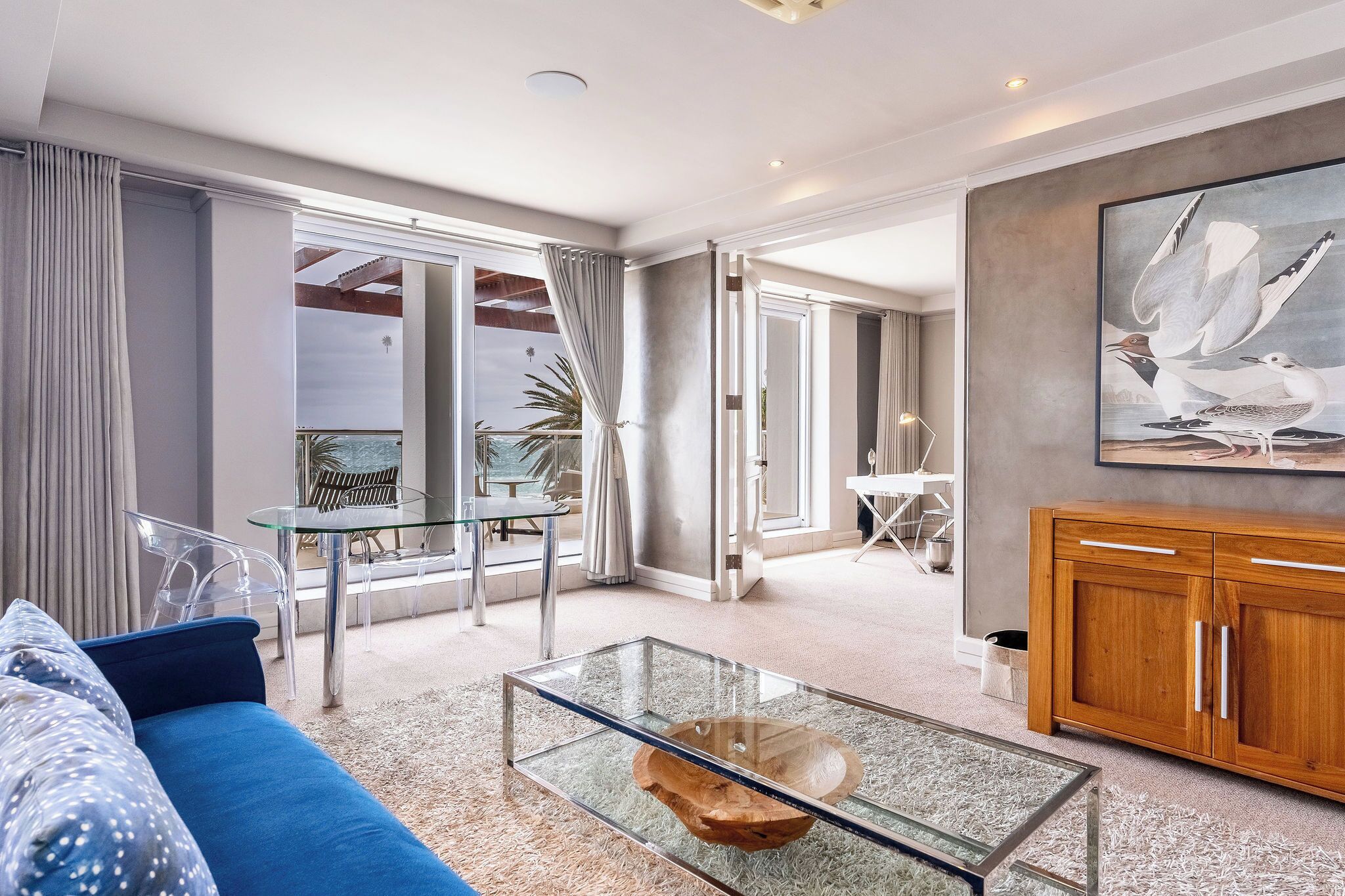 A modern living room with a glass coffee table, a blue sofa, and a wooden cabinet.