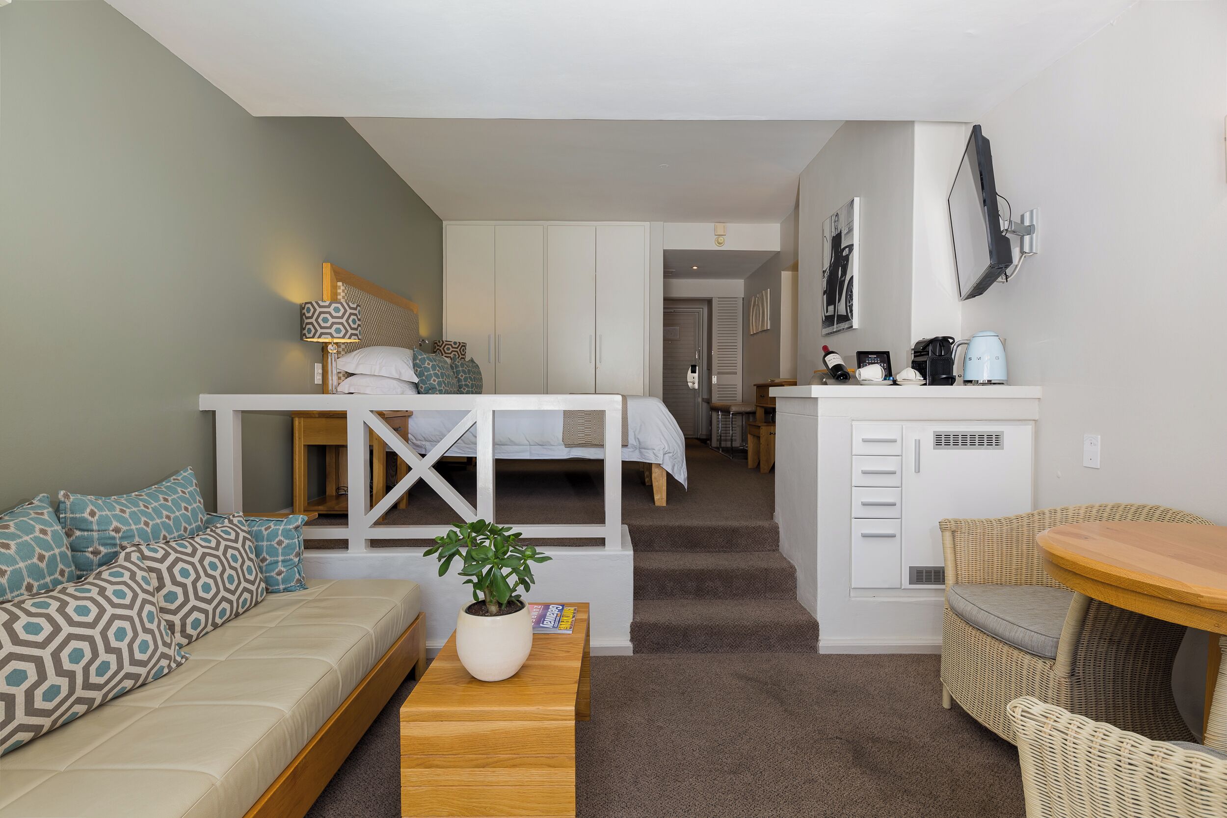 Quarto de hotel compacto com cama, sofá e uma pequena área de refeições.