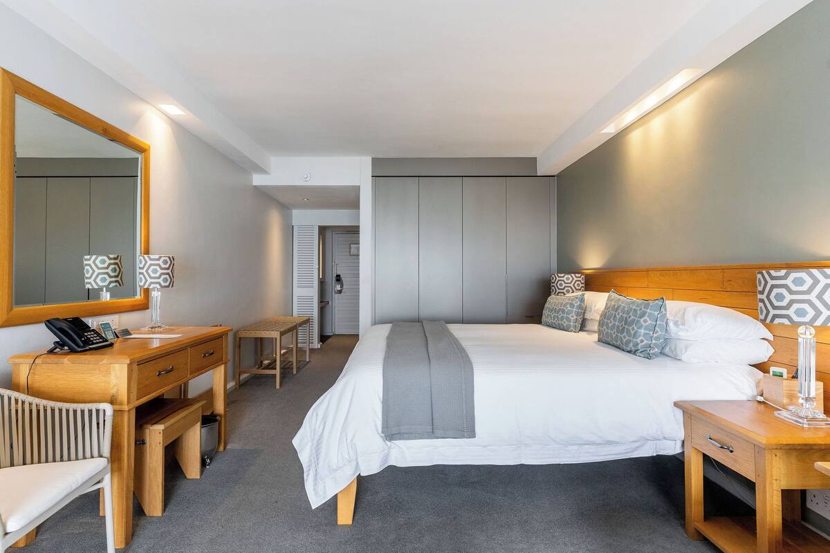 Ein modernes Hotelzimmer mit einem großen Bett, Nachttischen, einem Schreibtisch und einem Spiegel.