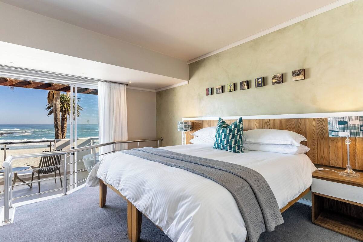 Ein Schlafzimmer mit einem großen Bett, einem Holzkopfstück, einem Nachttisch und Blick aufs Meer.