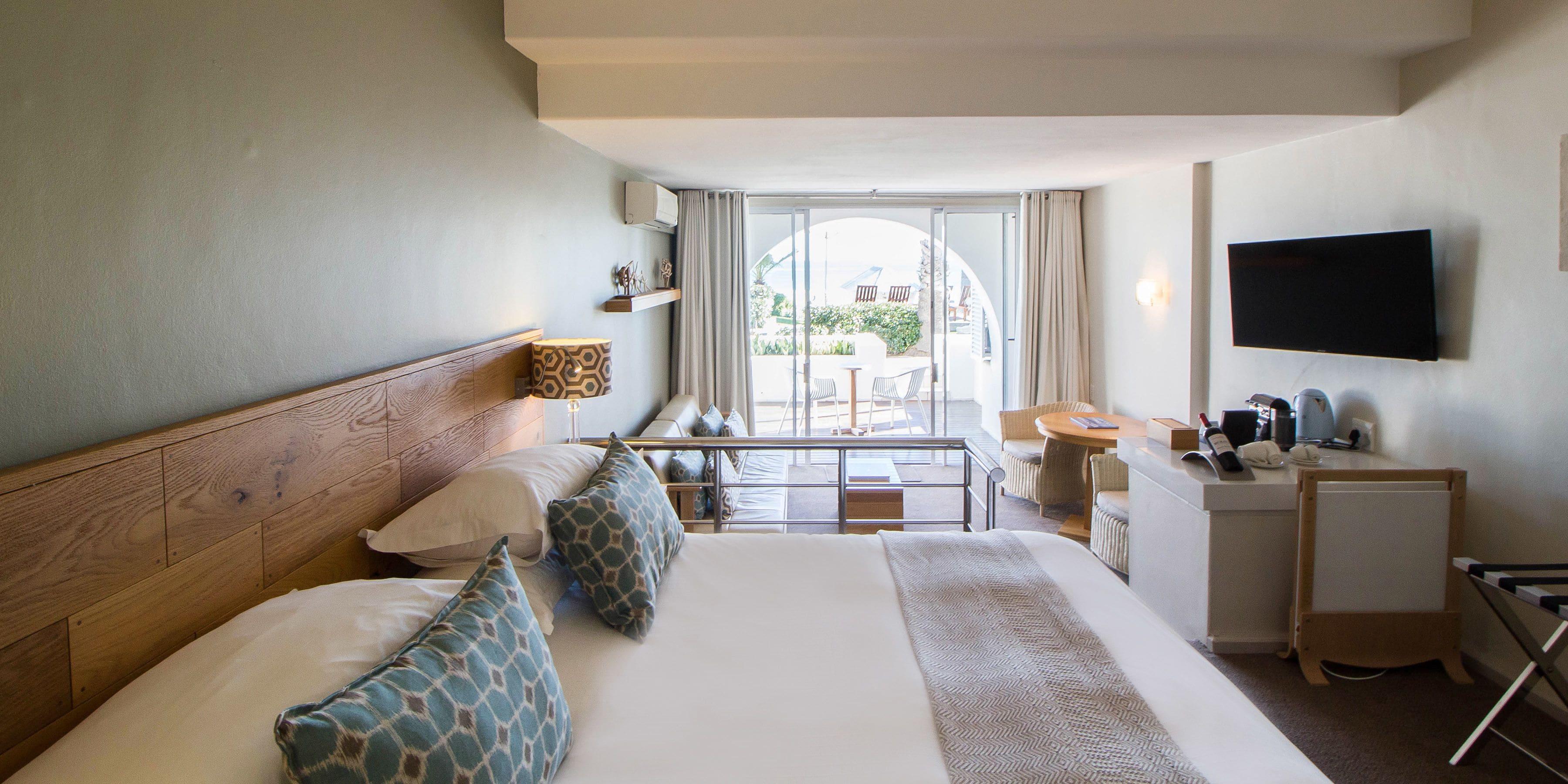 A hotel room with a large bed, a desk, a chair, a TV, and a view of the outdoors.
