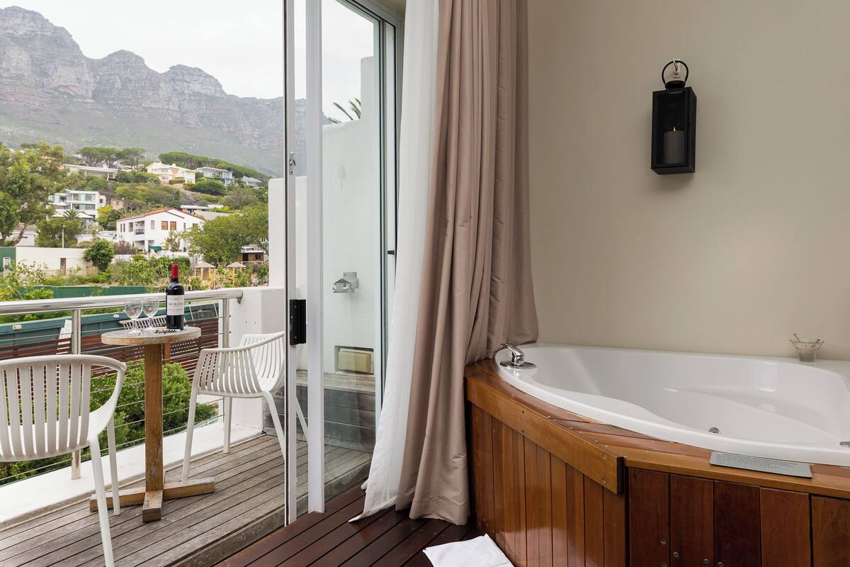 Ein Balkon mit Holzboden, weißen Stühlen, einem Tisch mit Flasche und Gläsern sowie einer großen weißen Badewanne.
