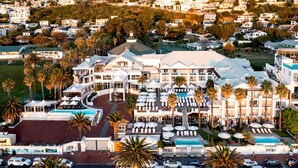 A large hotel with multiple floors, a swimming pool, and numerous outdoor umbrellas. - The Bay Hotel (Cape Town)
