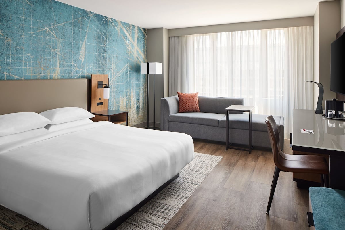 A hotel room with a large bed, a desk, a chair, a sofa, and a television.