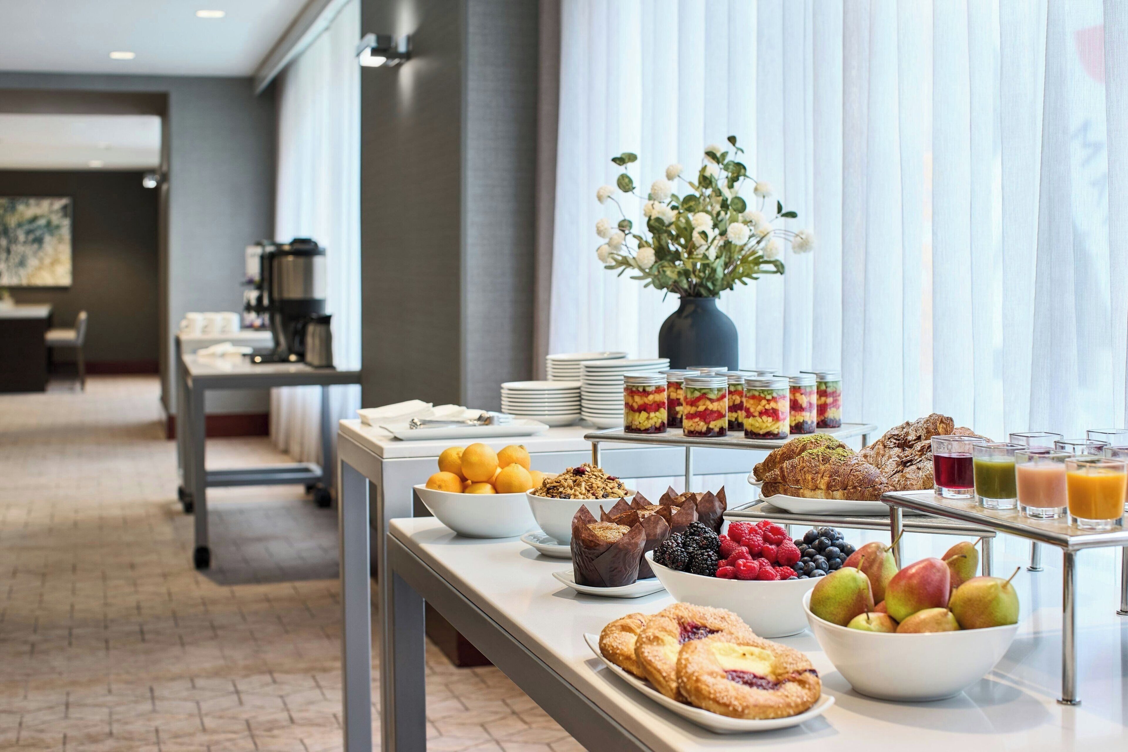 A buffet with various breakfast items including fruits, pastries, and beverages.