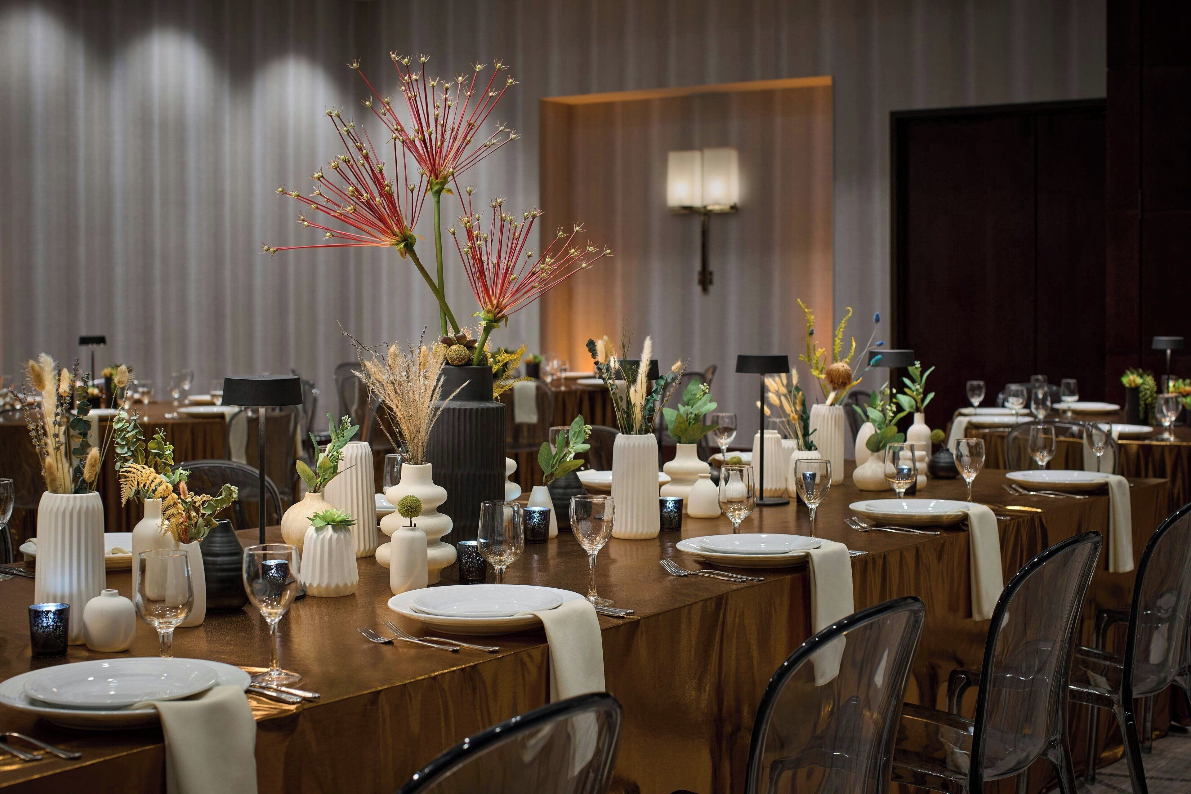 A long dining table set with white plates, clear glassware, and decorative vases with plants.