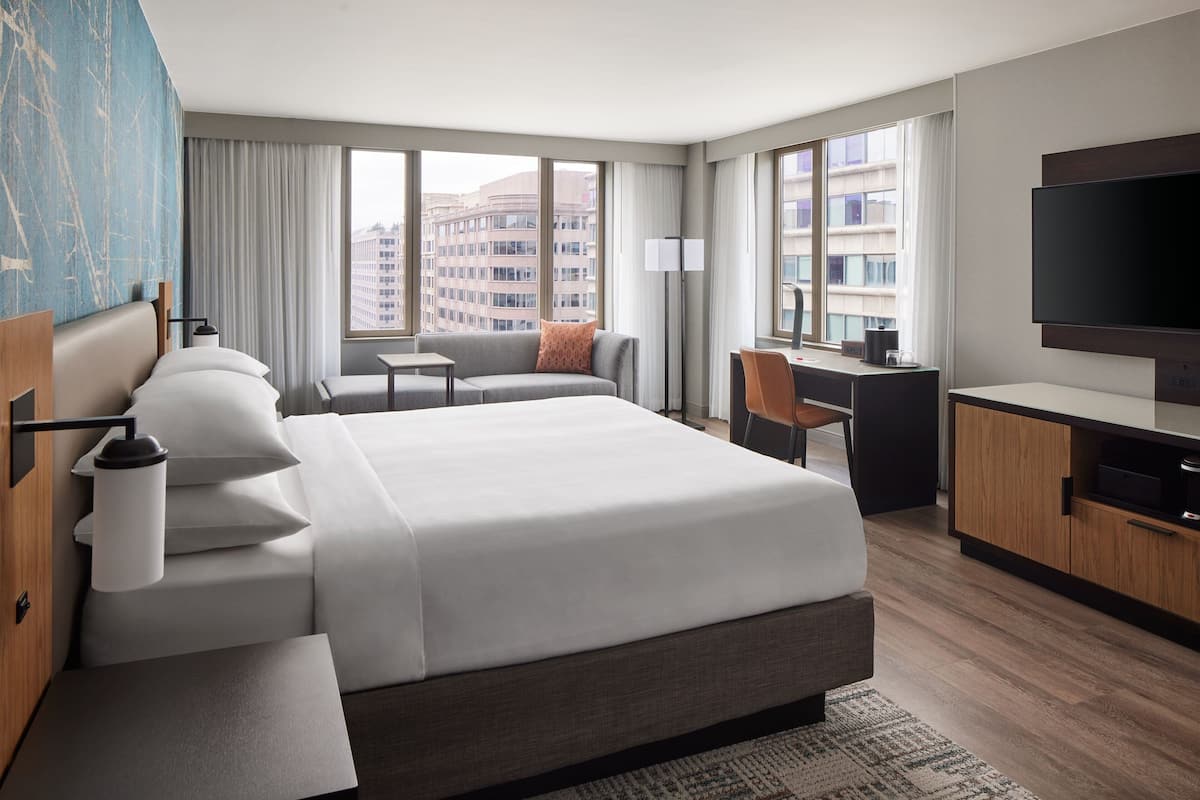 A modern hotel room with a large bed, a desk, a sofa, and a TV.