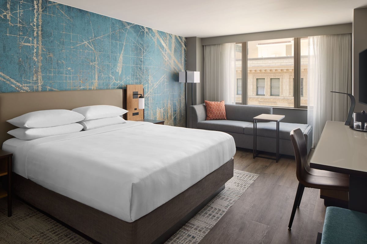 A hotel room with a large bed, a sofa, a small table, and a TV.