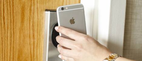 A hand using a smartphone to interact with a door lock.