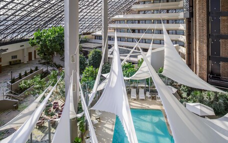 A high-rise hotel with a rooftop pool, indoor garden, and a view of the cityscape.