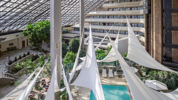A high-rise hotel with a rooftop pool, indoor garden, and a view of the cityscape. - DoubleTree by Hilton Rochester (Rochester)