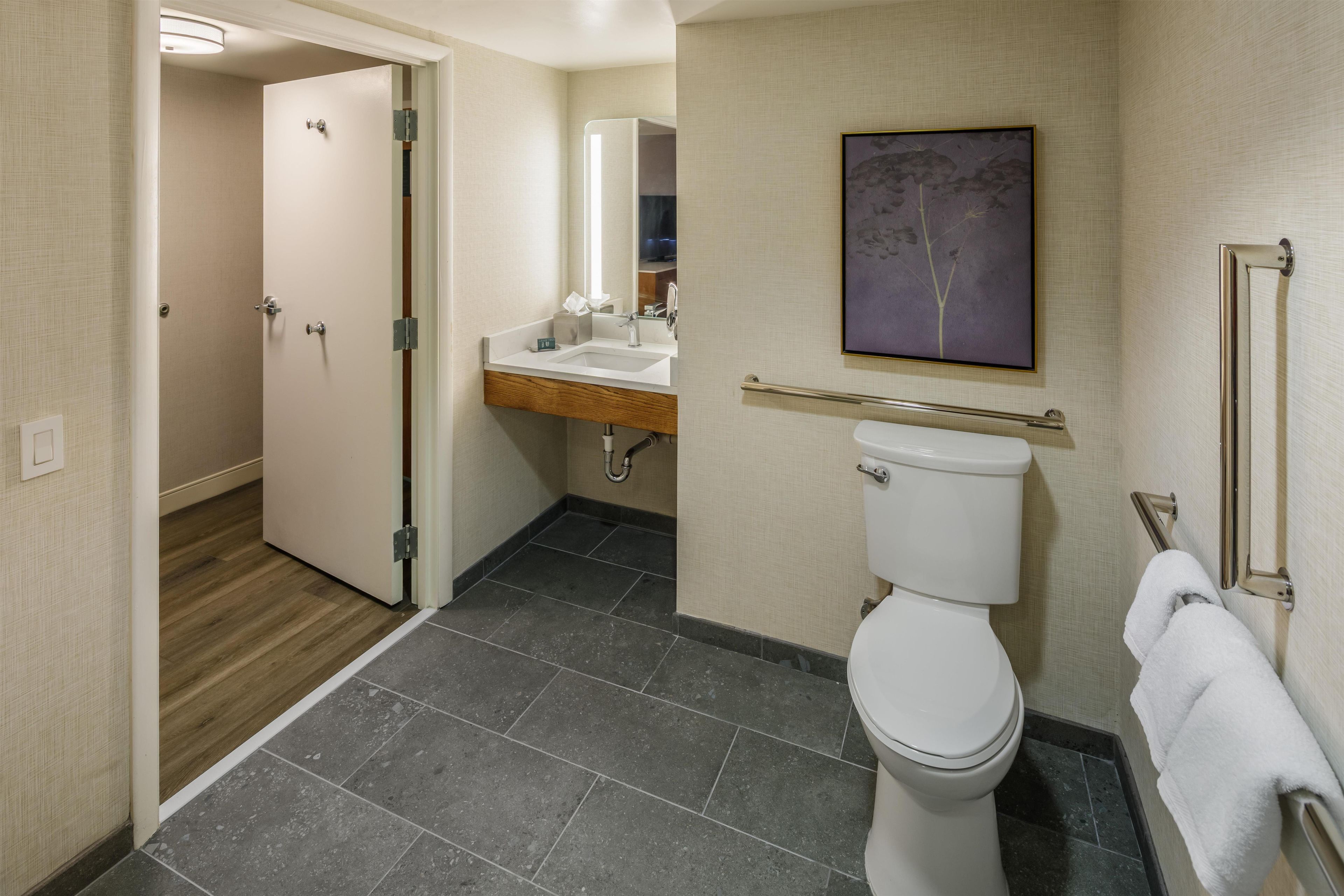 A hotel bathroom with a toilet, sink, and mirror.