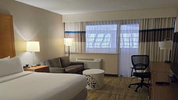 A hotel room with a large bed, a desk, a chair, a lamp, and a window with curtains.