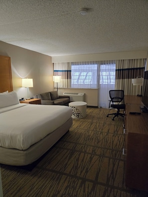 A hotel room with a large bed, a desk, a chair, a lamp, and a window with curtains. - DoubleTree by Hilton Rochester (Rochester)