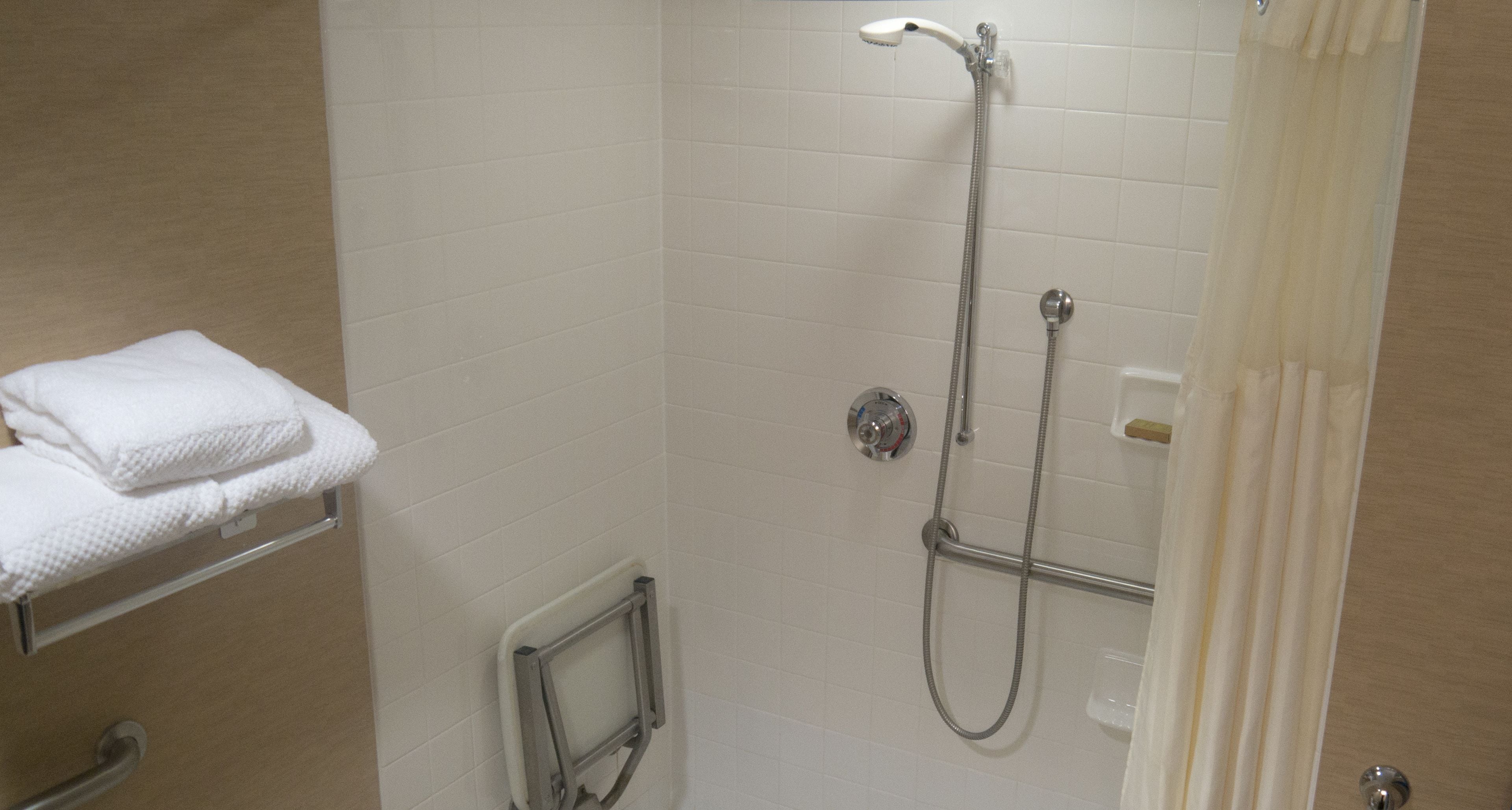 A shower with a handheld showerhead and a wall-mounted faucet, a towel rack with a folded towel, and a grab bar.