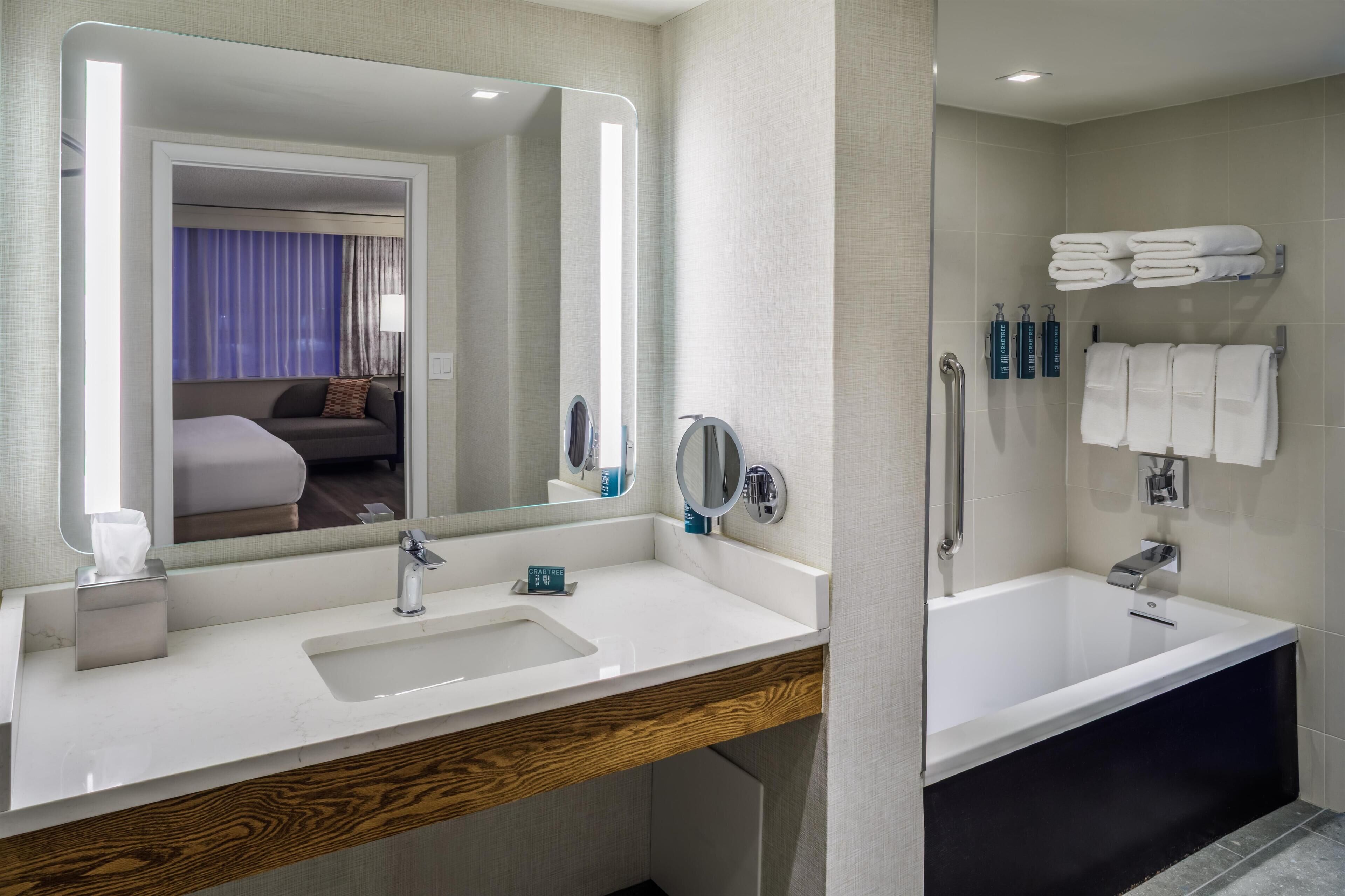 Un baño moderno con un espejo grande, un lavabo, una bañera y un perchero para toallas.