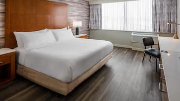 A hotel room with a bed, bedside table, lamp, chair, and a window with curtains.