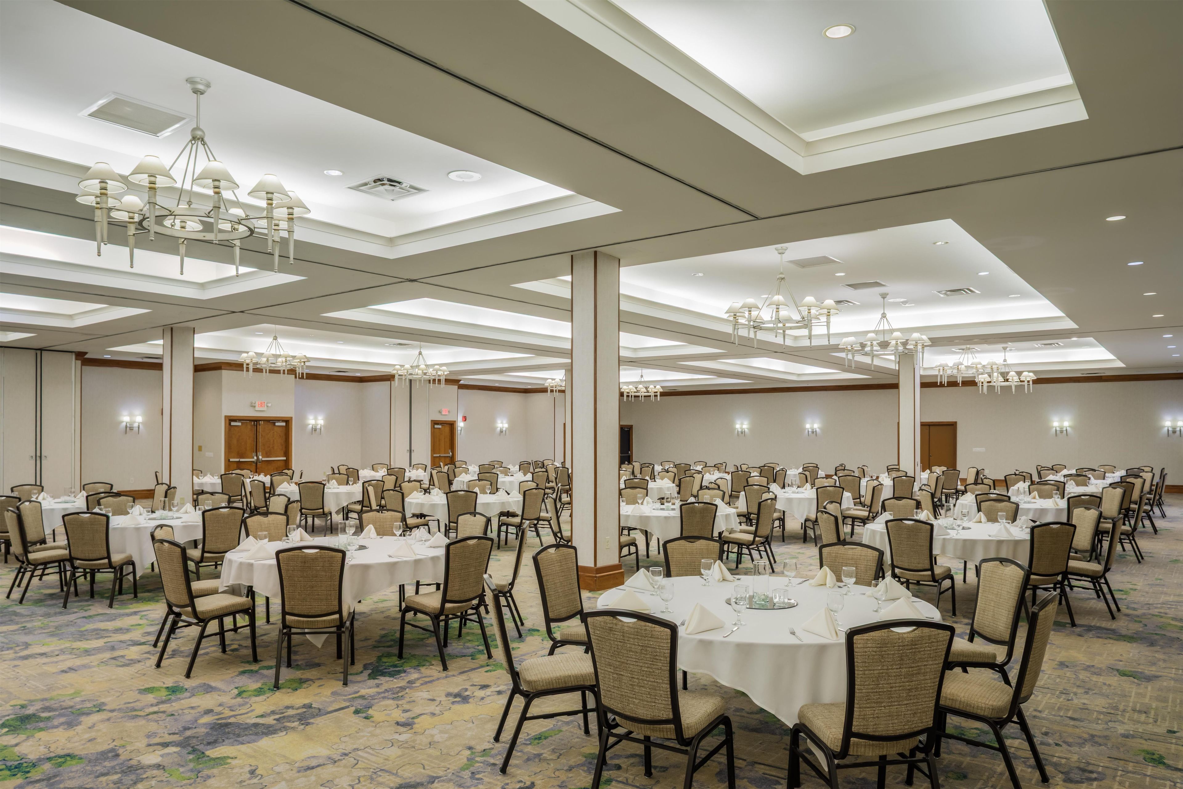 A large banquet hall with multiple round tables, chairs, and chandeliers.