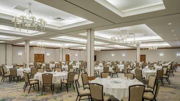 A large banquet hall with multiple round tables, chairs, and chandeliers.