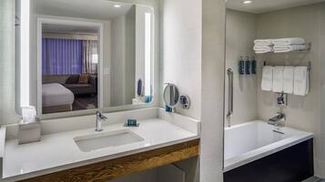 A hotel bathroom with a large mirror, a sink, a vanity, a bathtub, and a towel rack.