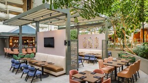 A modern outdoor seating area with tables and chairs, a bar in the background, and a pergola structure. - DoubleTree by Hilton Rochester (Rochester)