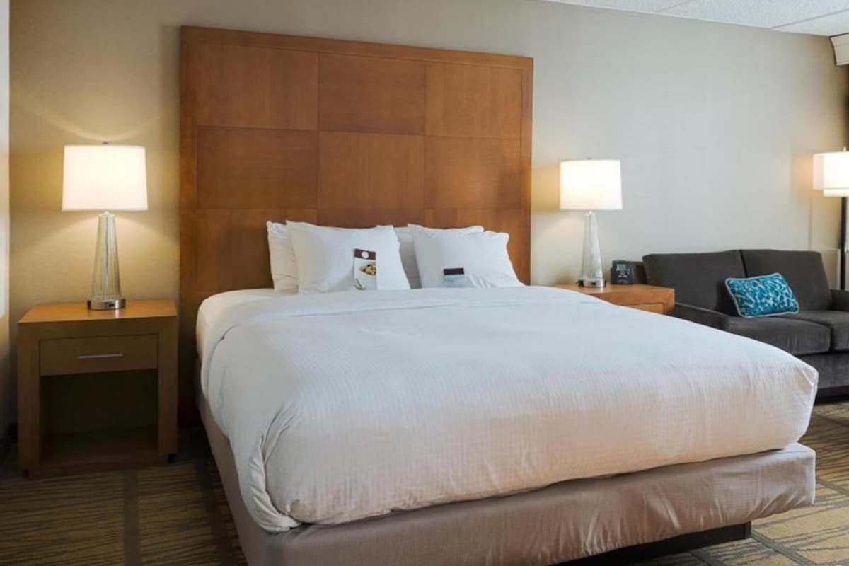 Una habitación de hotel con una cama grande, dos mesitas de noche, un sofá y dos lámparas.