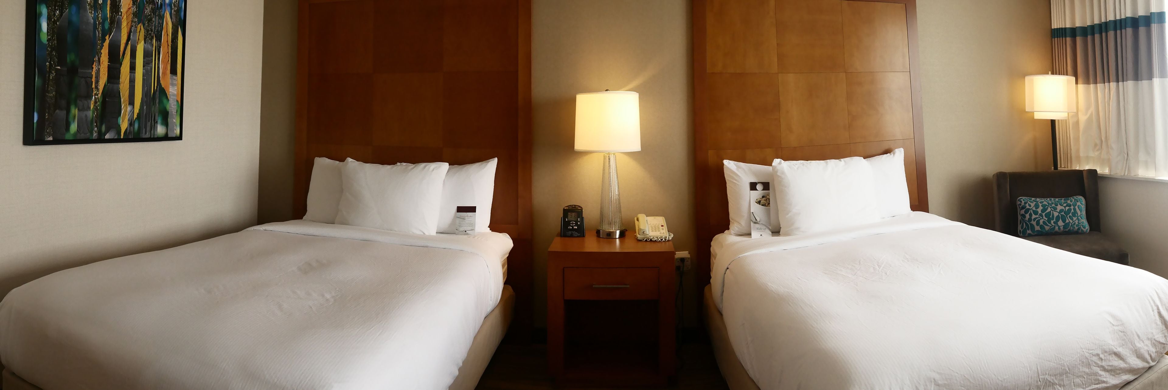 A hotel room with two beds, a nightstand with a lamp, a phone, and a small table.