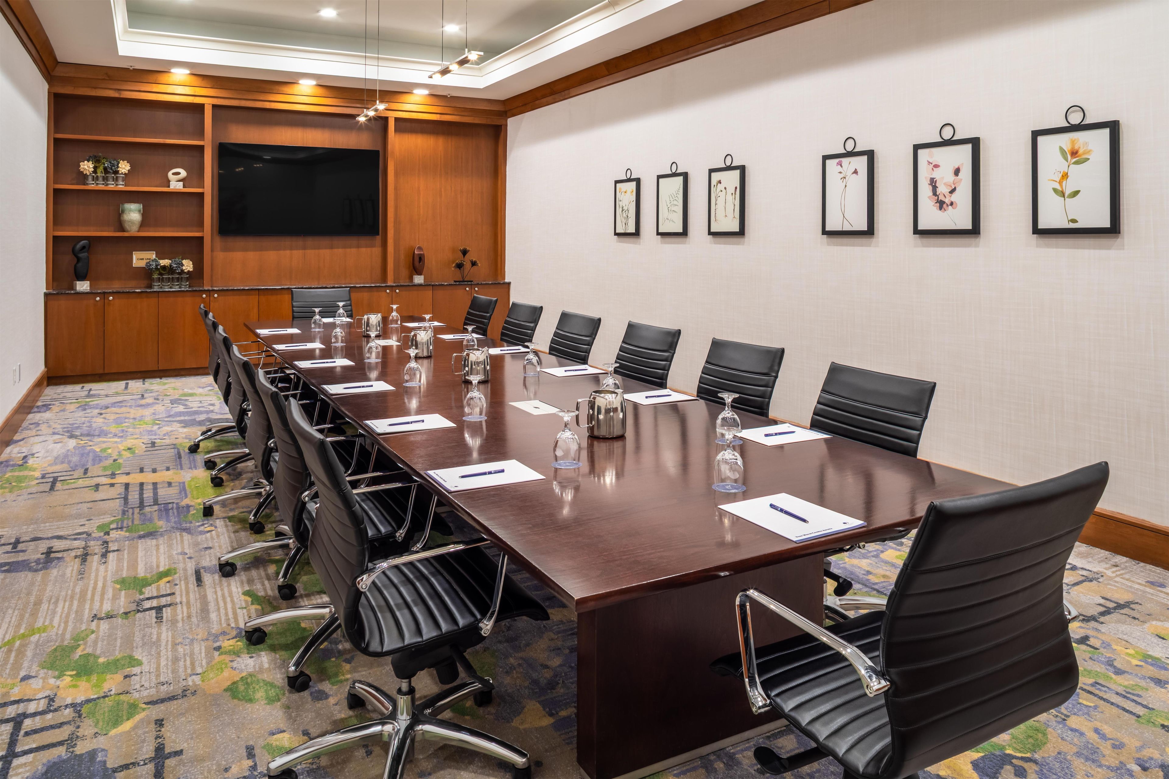A conference room with a long table, black chairs, and a television on the wall.