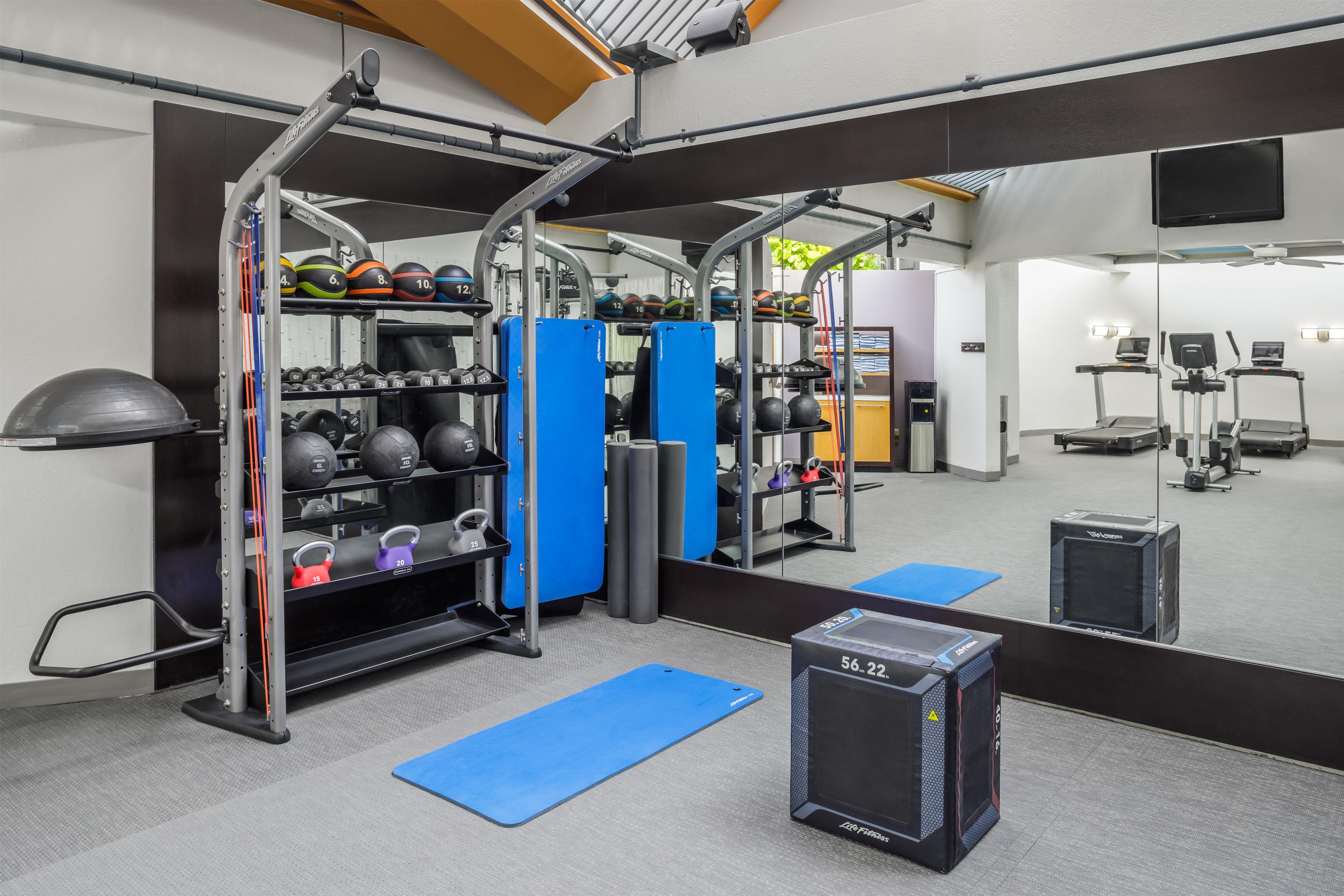 Un gimnasio con equipo de ejercicio, pesas y un espejo grande.