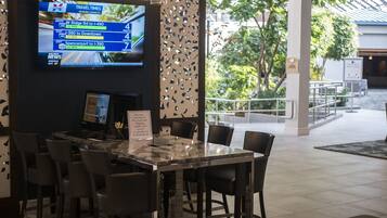 Eine Hotelhalle mit Empfangsschalter, Sitzgelegenheiten und einem großen Bildschirm, der Reisezeiten anzeigt.