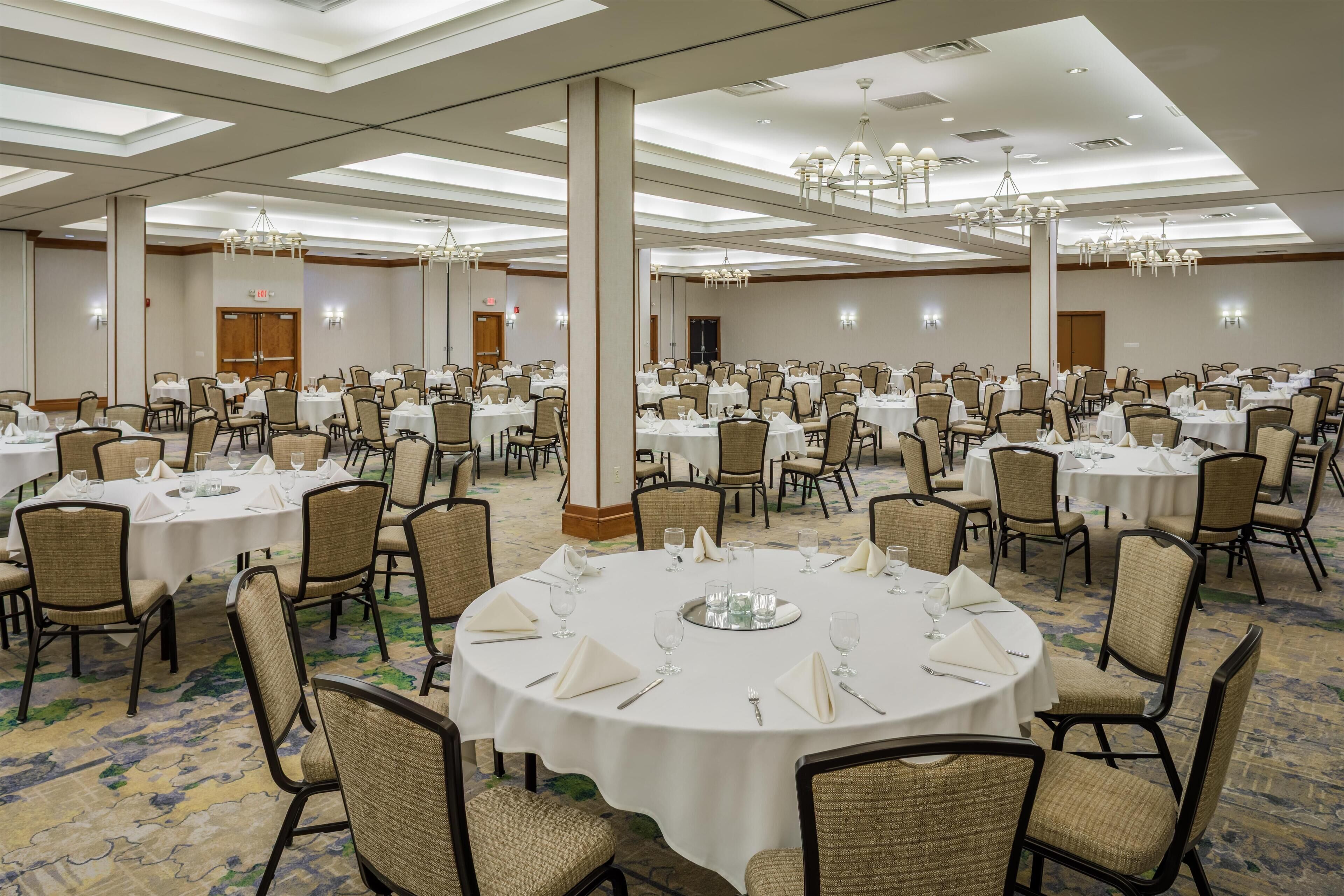 A large banquet hall with round tables, chairs, and chandeliers.