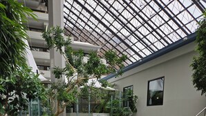 An indoor atrium with a patterned floor, large windows, and indoor plants. - DoubleTree by Hilton Rochester (Rochester)