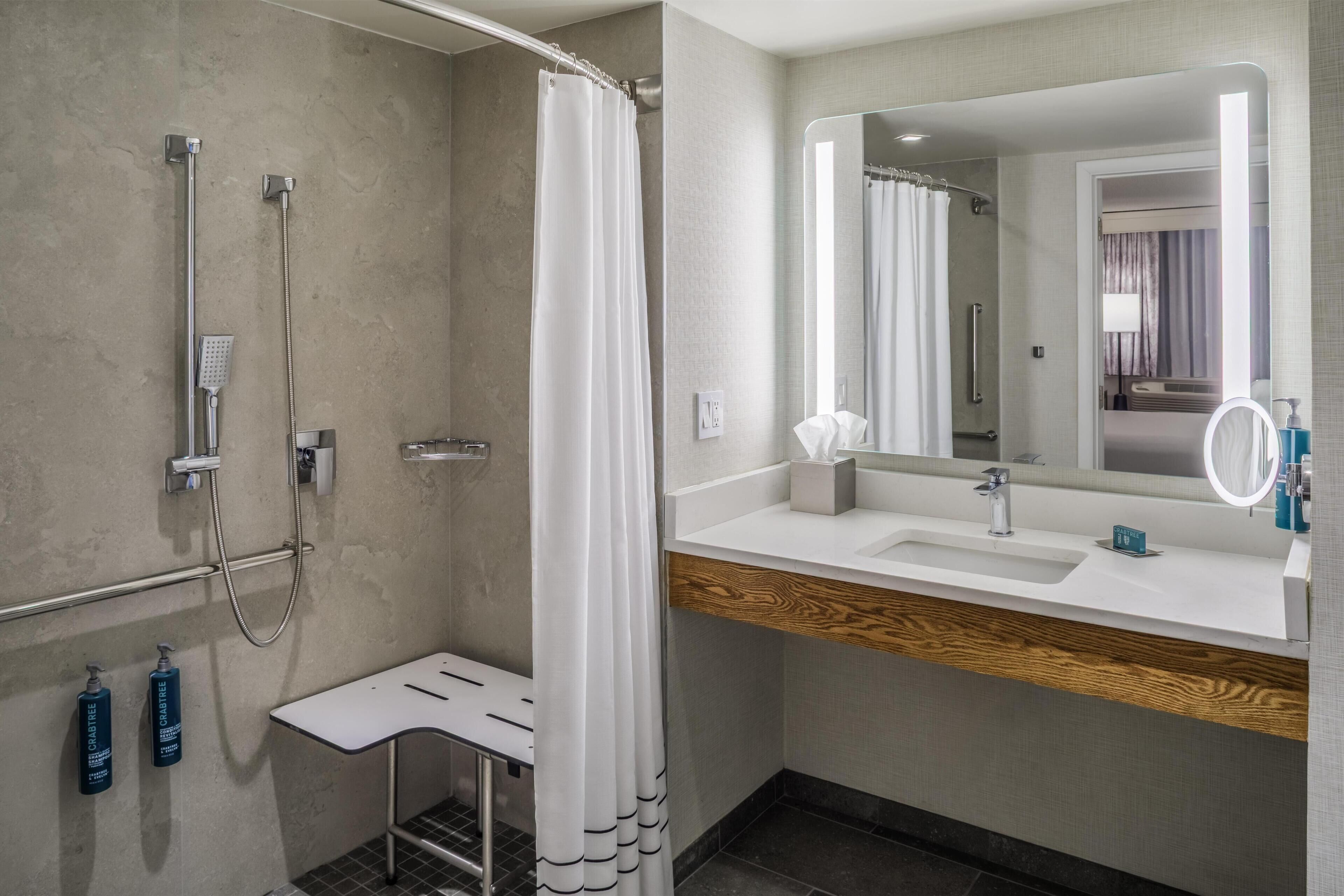 A modern bathroom with a shower, a sink, a mirror, and toiletries.
