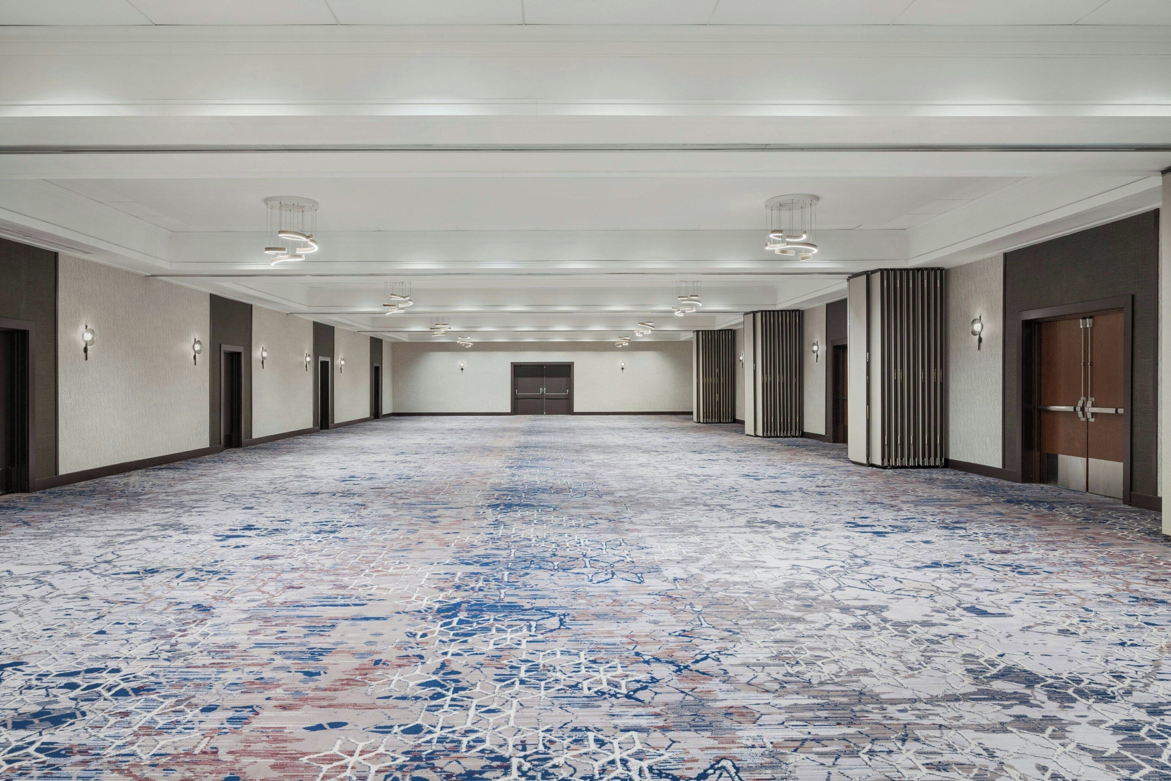 A long hallway with a patterned floor, doors on both sides, and recessed lighting on the ceiling.