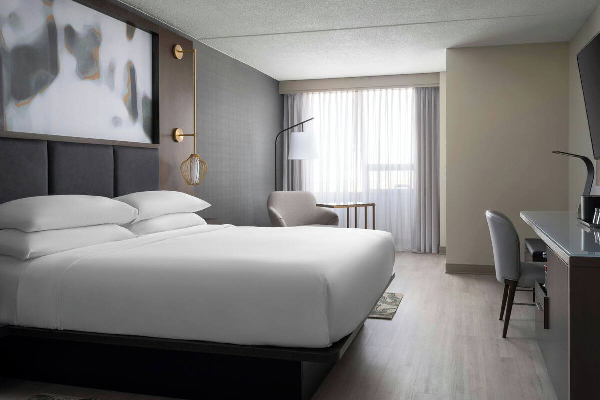 A modern hotel room with a large bed, a desk, and a chair.