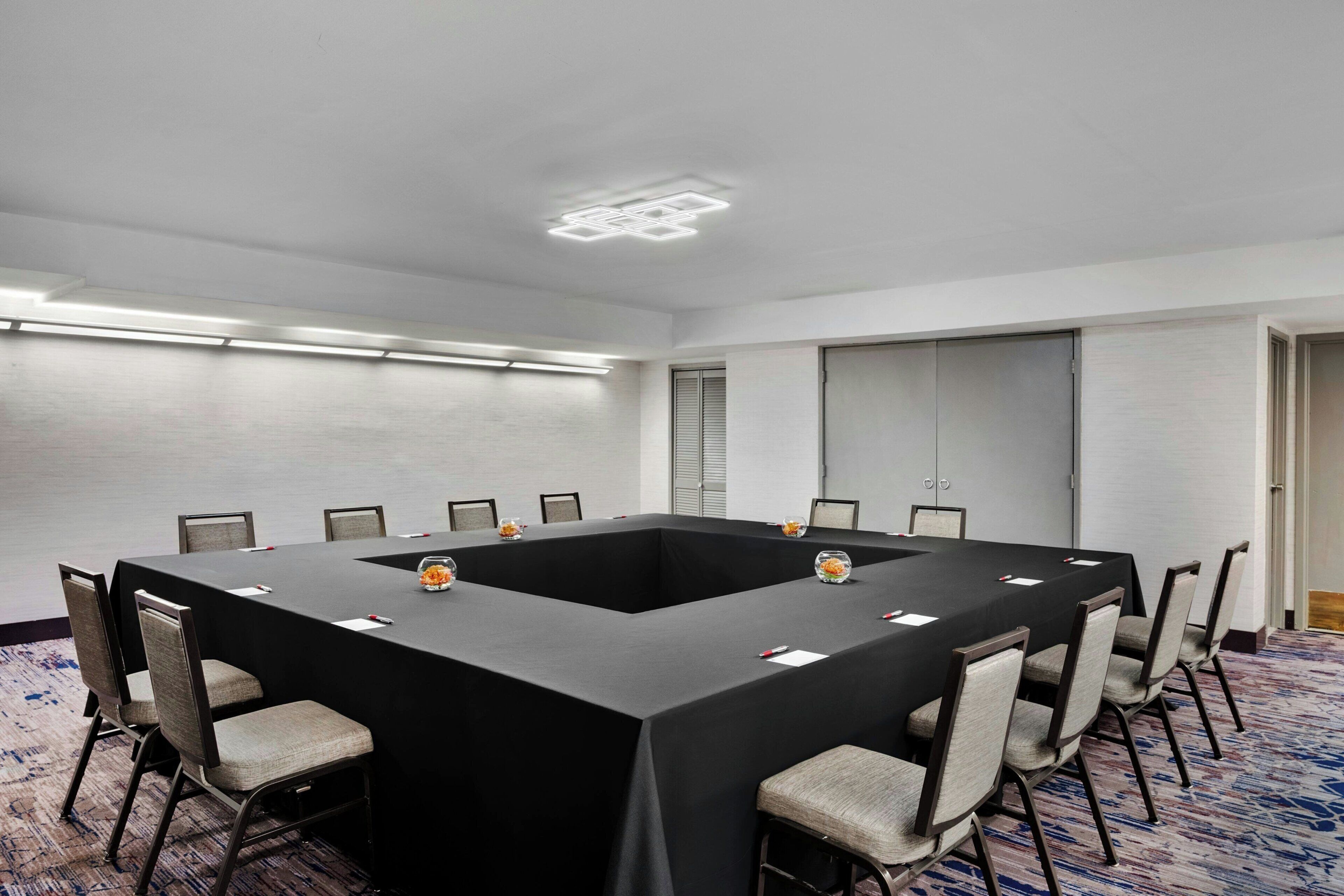 A conference room with a large rectangular table, multiple chairs, and a carpeted floor.