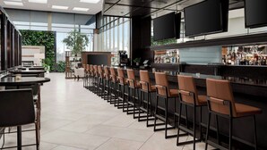 A modern bar area with high tables and bar stools, large windows, and a visible bar counter with various bottles. - Marriott Indianapolis East (Indianapolis)